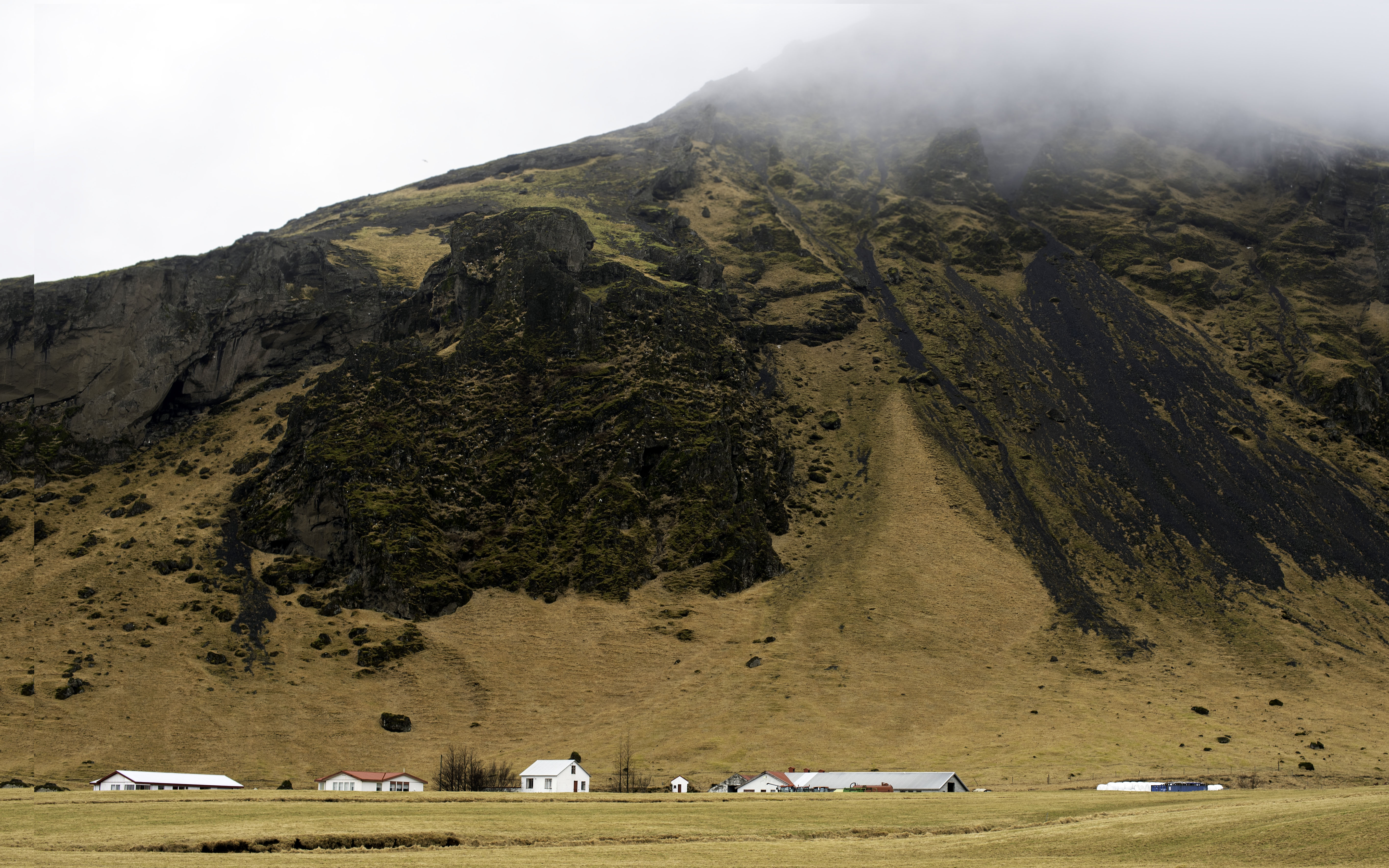 Iceland landscape with farm buildings beneath dramatic misty mountains